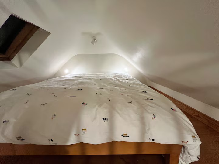 King-size bed under the sloping roof of the mezzanine, with a skylight and soft bedside lights